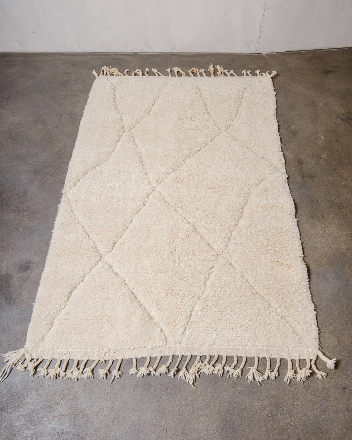 Cream wool rug with design woven in natural wool laying flat on concrete floor.